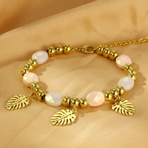 Detail of gold beaded bracelet with pink crystal beads and monstera leaf charms on silk