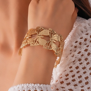 Close-up of a wide hollow butterfly cuff bracelet in gold finish worn on the wrist