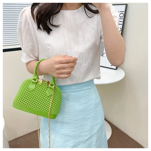 Green PVC shell handbag with gold chain strap shown being held by a model in casual wear