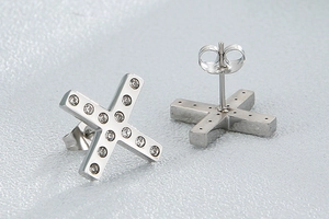 Macro view of silver cross earrings with embedded crystals and polished needle detail
