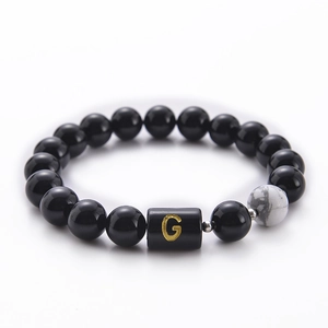Macro view of 10mm black agate beaded bracelet featuring a marble bead and golden letter G