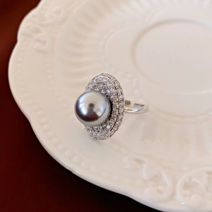 Macro view of a grey pearl ring with sparkling zircon halo on a white textured porcelain plate