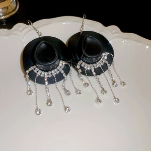Detail of cowboy hat earrings with sparkling rhinestone tassels on white ceramic tray