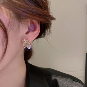 Detailopname van vergulde blad oorbellen met zirkonia en parels op model oor