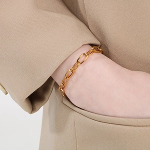 Detail of a bold gold rectangle link chain bracelet worn with a beige blazer outfit