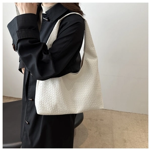 Détail du sac bandoulière blanc avec texture tissée porté par un mannequin sur un manteau noir