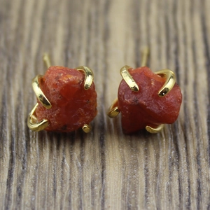 Macro shot of irregular orange raw mineral stones set in golden four-prong earrings