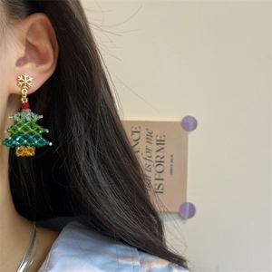 Detail of beaded Christmas tree earring with gold snowflake stud on model's ear