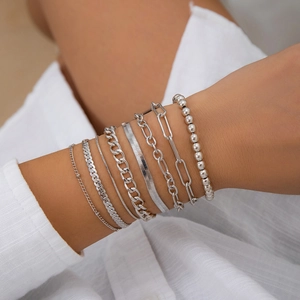 Detail of seven silver metal heart pendant beaded bracelets layered on a model's wrist