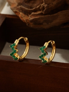 Close-up of gold hoop earrings with green zircon inlay on a dark wooden stand