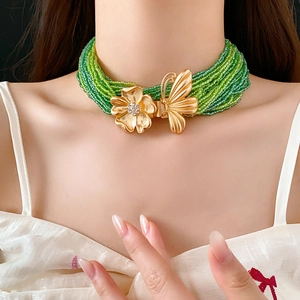 Detail of green beaded multilayer necklace featuring gold butterfly and rhinestone flower