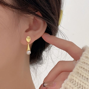Close-up of elegant gold pearl drop earring worn by model with minimalist knitwear