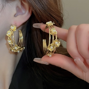 Detail of gold triple-hoop earrings featuring delicate floral motifs and inlaid pearls