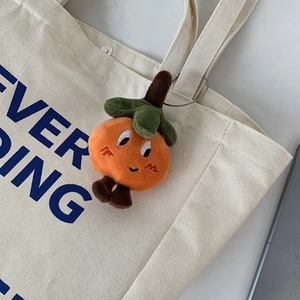 Close-up of a smiling orange plush persimmon keychain on a beige canvas tote bag