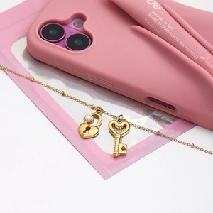 Collier doré avec pendentifs cœur et clé, détail perle, présenté dans un décor rose élégant