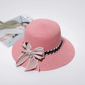 Detail of pink woven straw sun hat with wavy ribbon, elegant bow, and pearl accent
