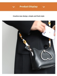 Detail of woven crossbody strap and heart-shaped metal buckle on black leather phone bag