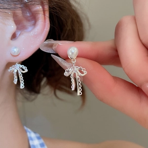 Detailed close-up of bow-knot pearl pendant earring on ear for scale and texture