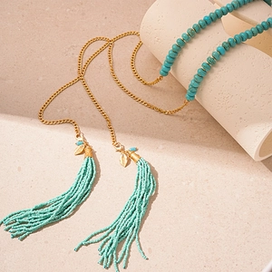 Détail macro du collier en perles turquoise avec breloques feuilles dorées et pompons