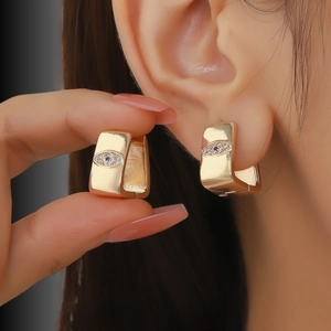 Detail view of gold wide band hoop earrings with blue zircon evil eye charm on ear