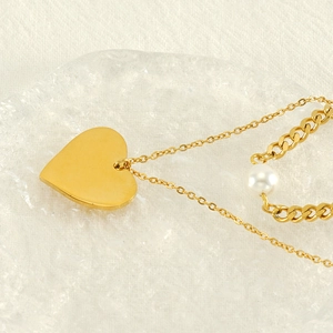 Double-layered gold heart pendant necklace with pearl detail on a textured glass display