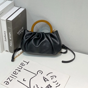 Black ruched leather cloud bag with wooden handle and gold chain strap on white desk