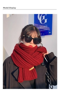 Detail of red knit scarf with handmade leather tag worn by model in casual style