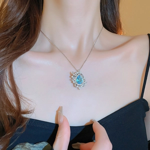 Close-up of a teardrop-shaped blue gemstone pendant on a pearl necklace for women