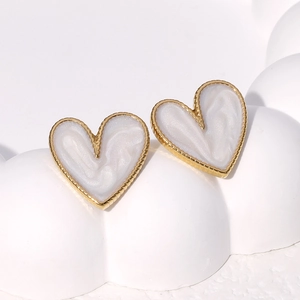 Detail of heart-shaped gold studs with creamy pearl inlay on a white platform