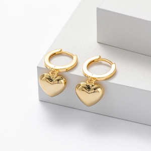Macro shot of polished gold heart pendant earrings on a minimalist geometric pedestal