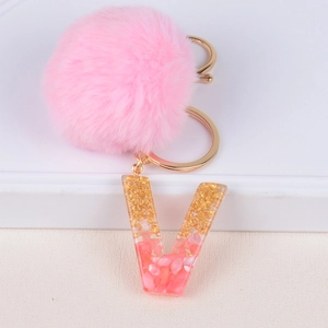 Pink fur ball keychain with golden foil resin letter V on a modern white display