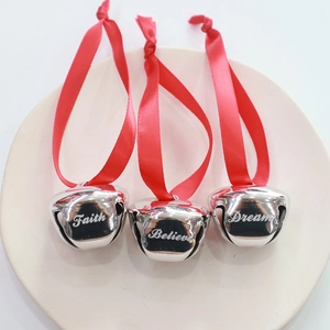 Three silver 38mm Christmas bells with red ribbons and engraved holiday words on a tray