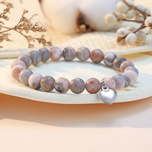 Close-up of pink and grey natural stone bead bracelet with silver heart charm on white plate