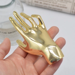 Polished gold-tone hand-shaped brooch held in palm against a blurry newspaper backdrop