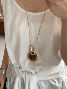 Detail of a large gold teardrop pendant on a snake chain worn on a white tank top