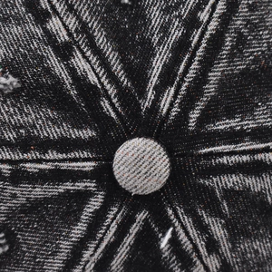 Macro shot of washed black distressed denim baseball cap top button and radial stitching