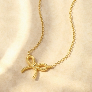 Gros plan du collier avec pendentif nœud doré torsadé sur fond de tissu doux