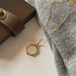 Detail view of a gold shell necklace styled with a leather wallet and grey sweater