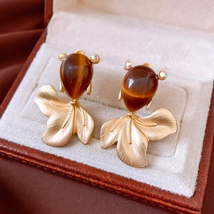 Close-up of golden fish earrings with brown stones on a beige velvet jewelry box