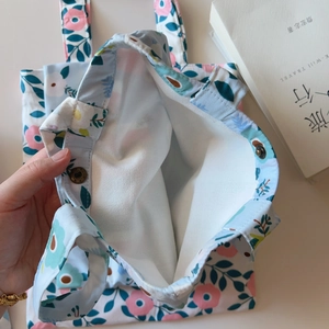 Detailed close-up showing the metal magnetic buckle and floral lining of the small canvas bag