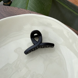 Close-up of matte black 5.5cm hair claw clip on a ceramic plate with natural decor
