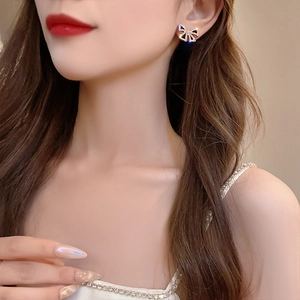 Macro shot of s925 gold bow earrings with black and blue rhinestones on a model ear