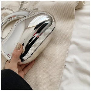 Close-up of a silver curved metal clutch bag with a high-gloss finish on beige fabric