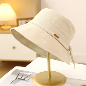 Detail of a chic beige cotton bucket hat with a bow and small metal tag on a stand