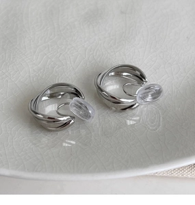 Détail de boucles d'oreilles clips géométriques argentées sur assiette céramique