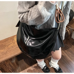 Detail of black patent leather hobo bag with vintage buckle on a grey knit outfit