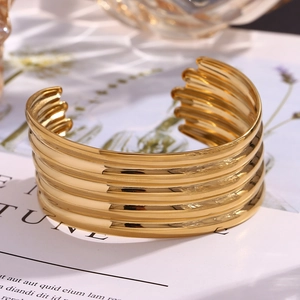 Detailed view of wide 18K gold plated multi-layer open cuff bracelet on a magazine backdrop