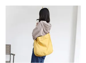 Detail view of large yellow canvas shoulder bag with leather strap and snap closure
