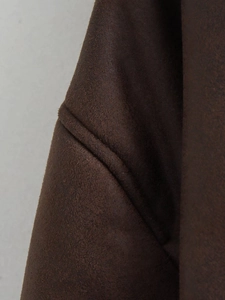 Macro shot of dark brown suede jacket fabric showing fine texture and premium stitching