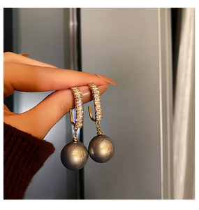 Gros plan de boucles d'oreilles dorées avec oxydes de zirconium et perles gris foncé